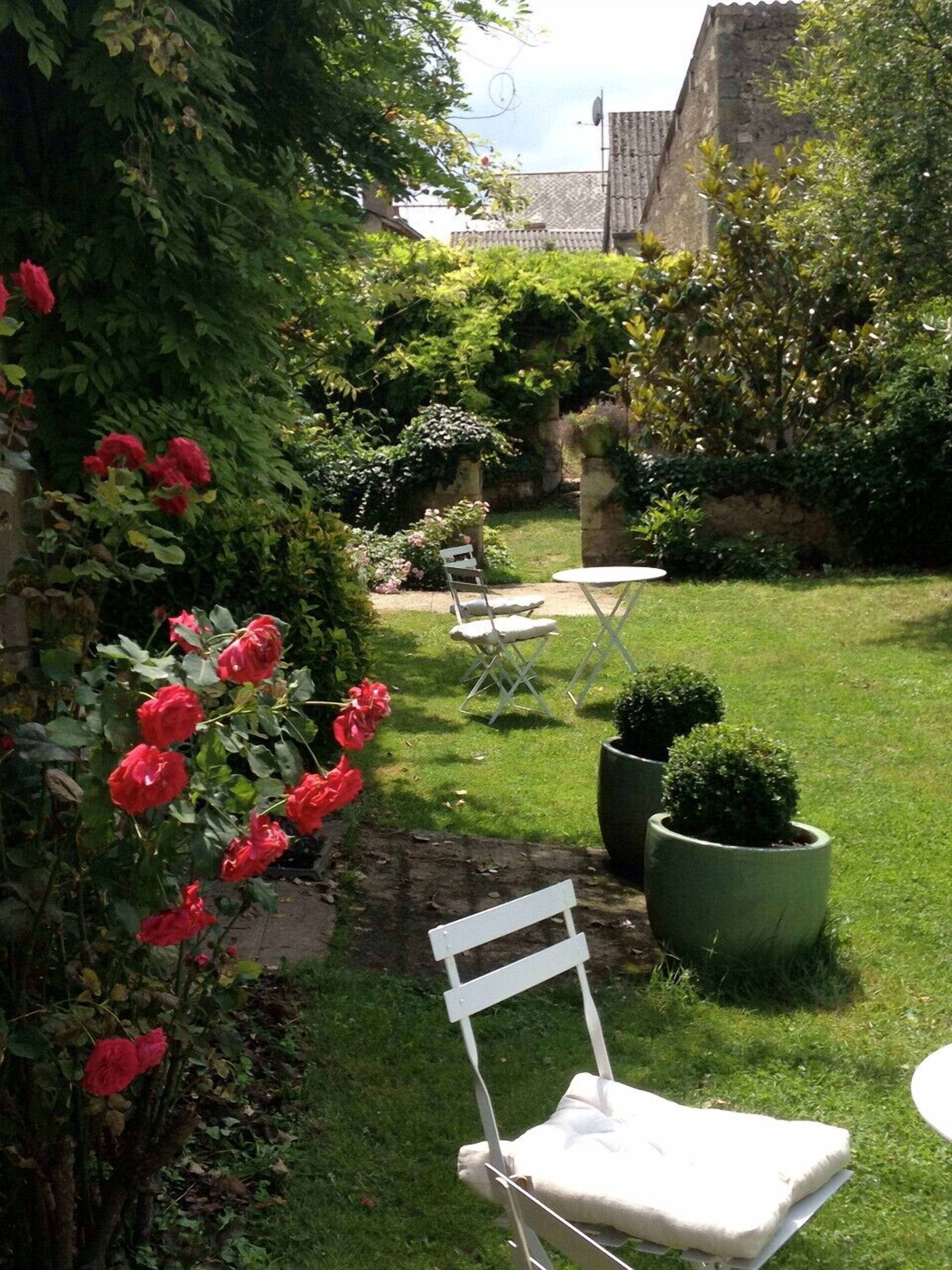 A garden with a lawn, a white chair, a small table, and a potted plant.