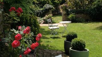 A garden with a lawn, a white chair, a small table, and a potted plant.
