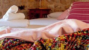 Et hotelværelse med en stenvæg, en seng med et pink sengetæppe, et trænatbord med en lampe og en stak farverige håndklæder.