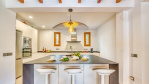 A modern kitchen with a central island, stainless steel appliances, and a unique pendant light. - Sustainable Finca Can Tomeu in Mallorca (Llubi)