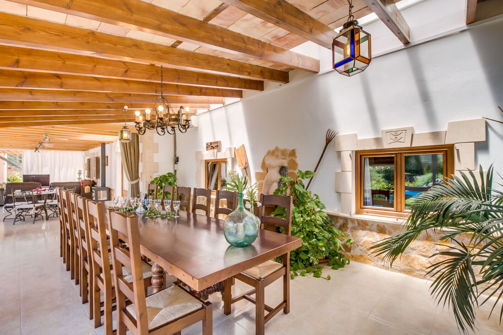 A spacious dining area with a wooden table and chairs, a chandelier, and a view of the garden through a window.