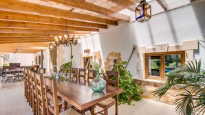 A spacious dining area with a wooden table and chairs, a chandelier, and a view of the garden through a window. - Sustainable Finca Can Tomeu in Mallorca (Llubi)