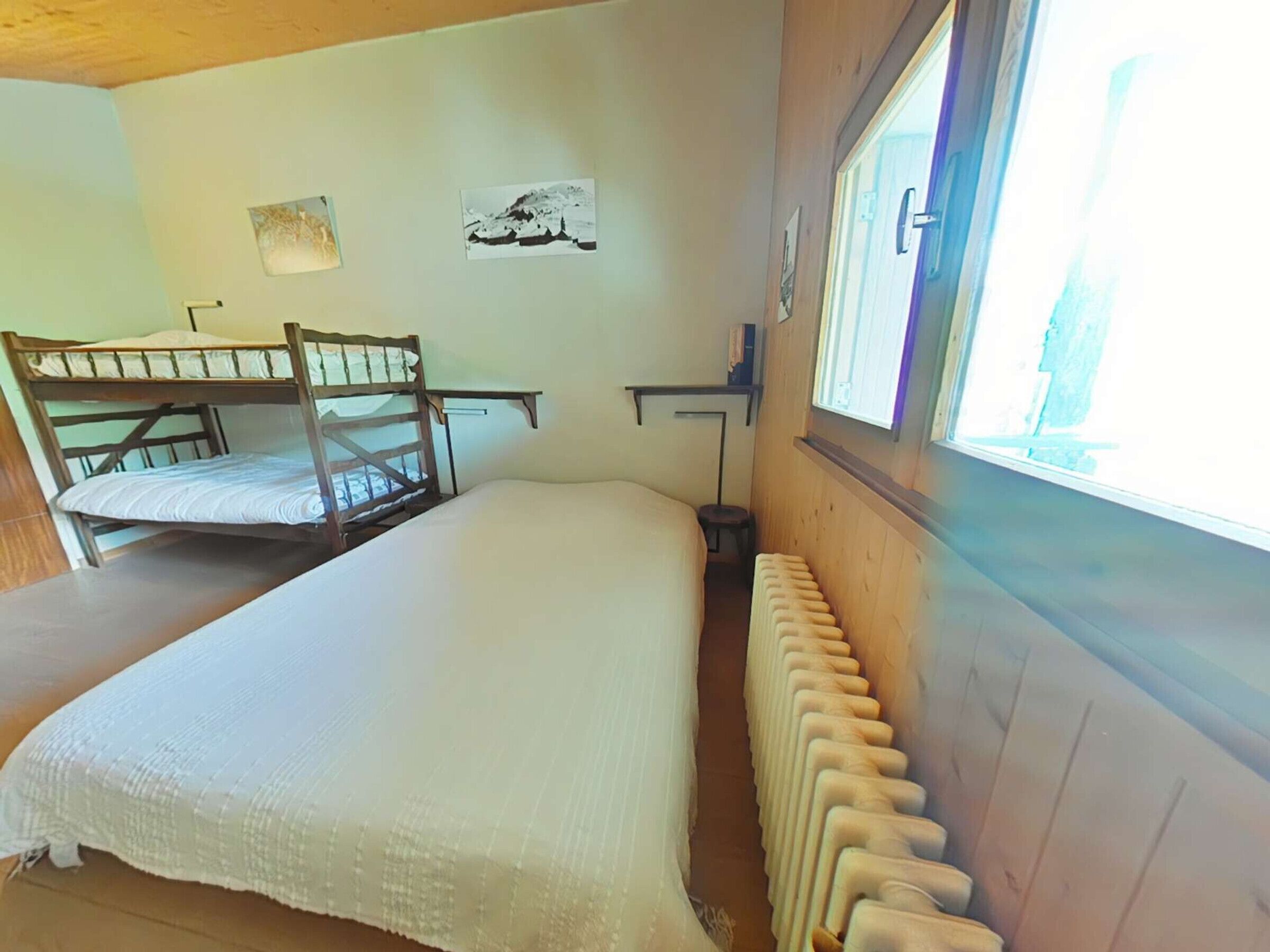 Camera con letto a castello, finestra, termosifone e un piccolo tavolo.