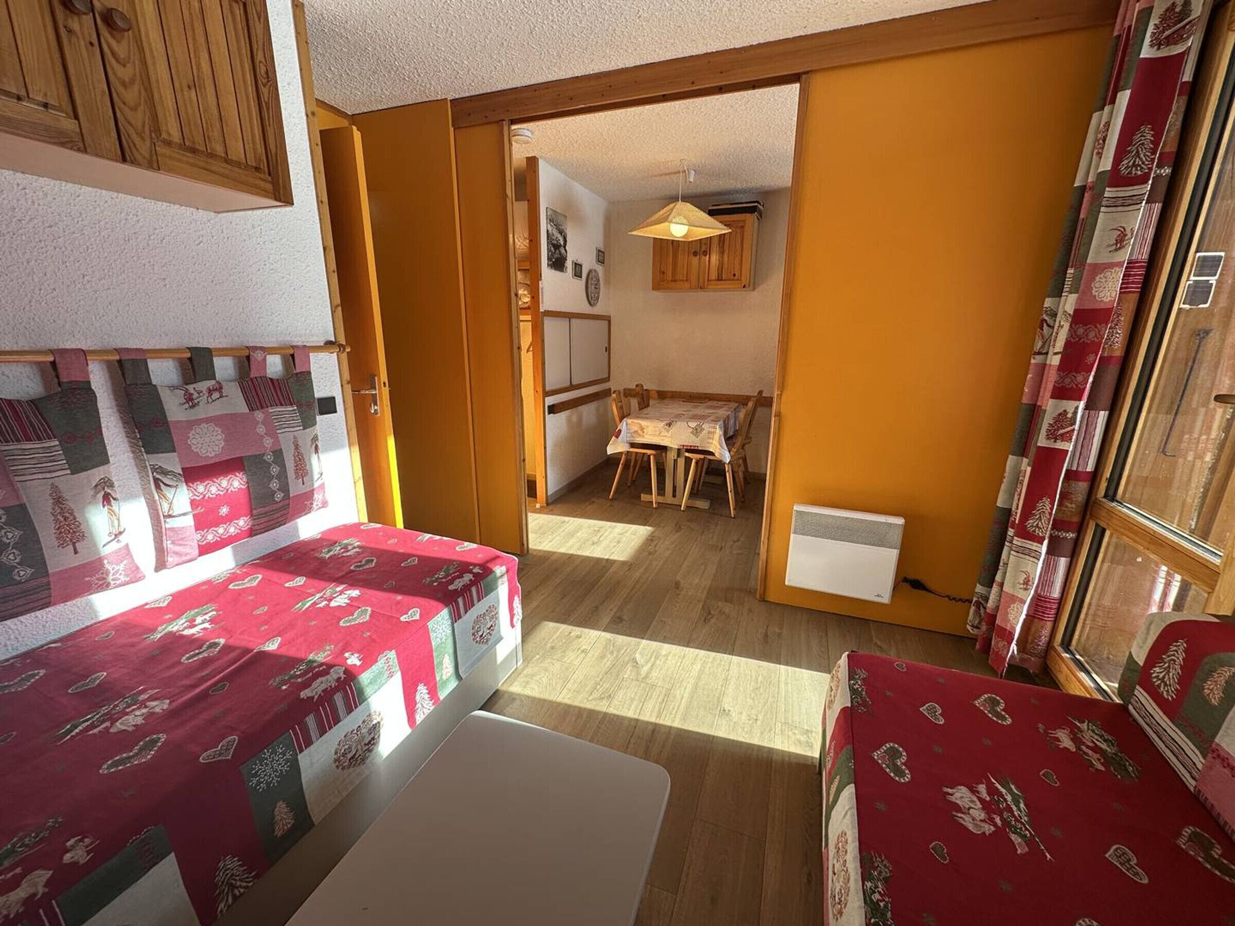 A cozy room with two beds, a small table, and a kitchenette.