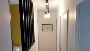 Ein schmales Korridor mit Holzboden, einer gerahmten Karte an der Wand und einem Bett mit gemustertem Überwurf im Hintergrund.
