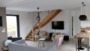 Ein modernes Wohnzimmer mit einer Holztreppe, einem Flachbildfernseher und einem Essbereich mit Tisch und Stühlen.