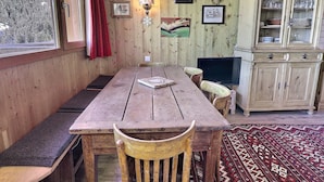 Una mesa de madera para comer con bancos, un televisor y un aparador con puertas de vidrio.