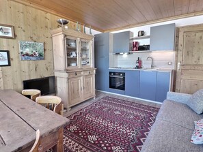 A compact kitchen with a built-in oven, a coffee maker, and a sink. There is a dining area with a wooden table and chairs.