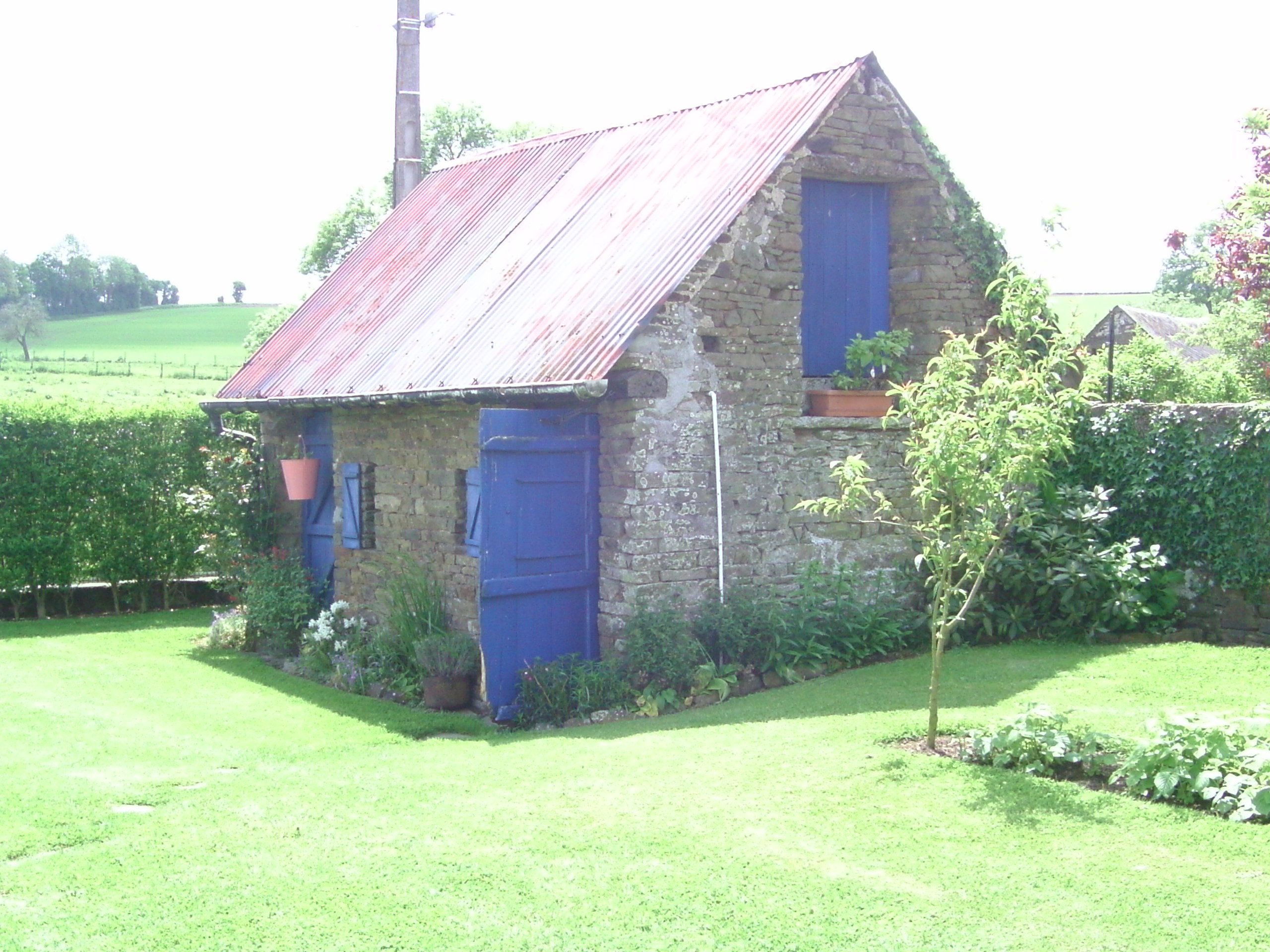 A stone house with a red roof, blue shutters, and a small garden area.