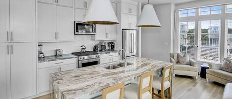 Uma cozinha moderna com armários brancos, uma ilha de mármore e iluminação pendente.