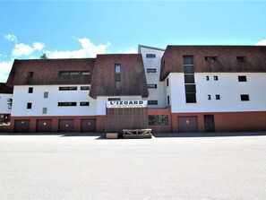 Um edifício com uma placa indicando "L'IZOARD". Possui vários andares, um telhado plano e diversas janelas.