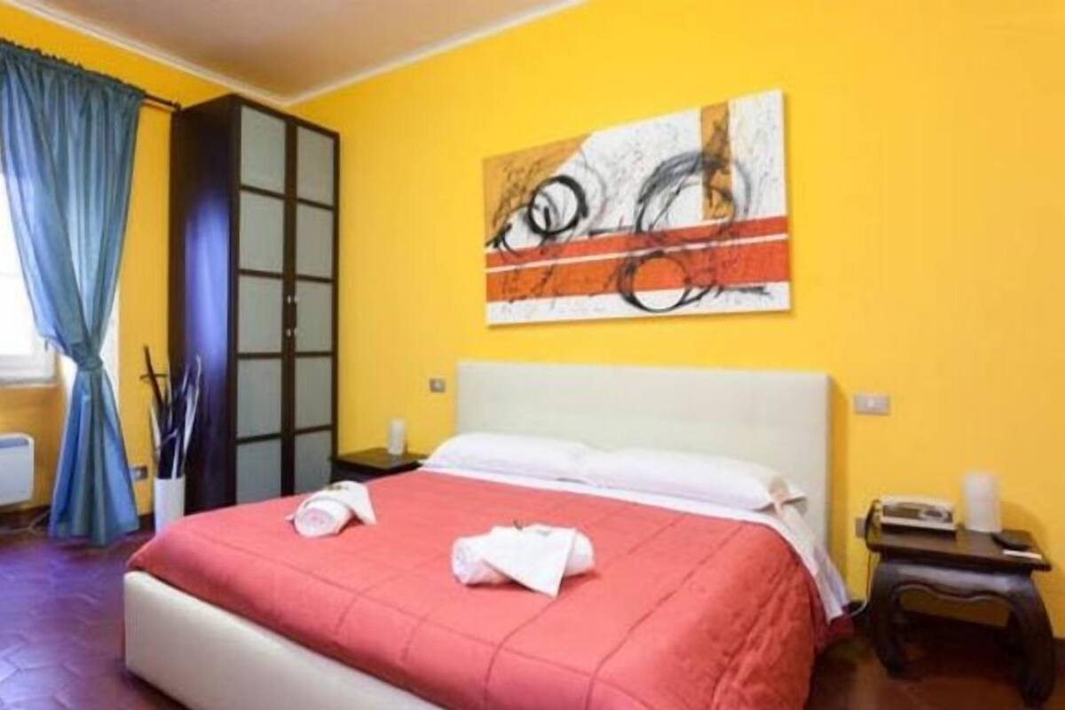 Una habitación de hotel con una cama, una mesita de noche, una ventana con cortinas y un cuadro en la pared.