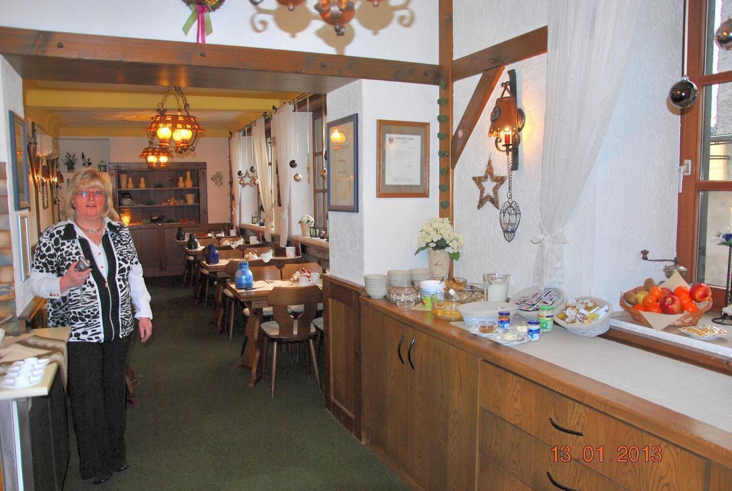Un restaurante con vigas de madera y candelabros, una barra de buffet con diversos alimentos, y una persona de pie al frente.