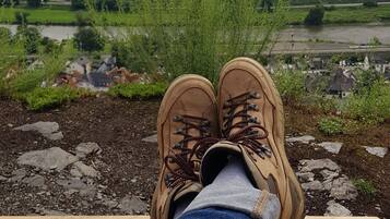 Un paio di scarponcini da trekking su una panca di legno con vista su un paesaggio rurale con case e campi.