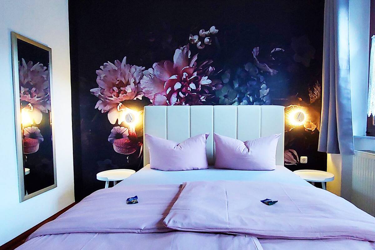 A bedroom with a large bed, two bedside tables, and a wall mural of flowers.