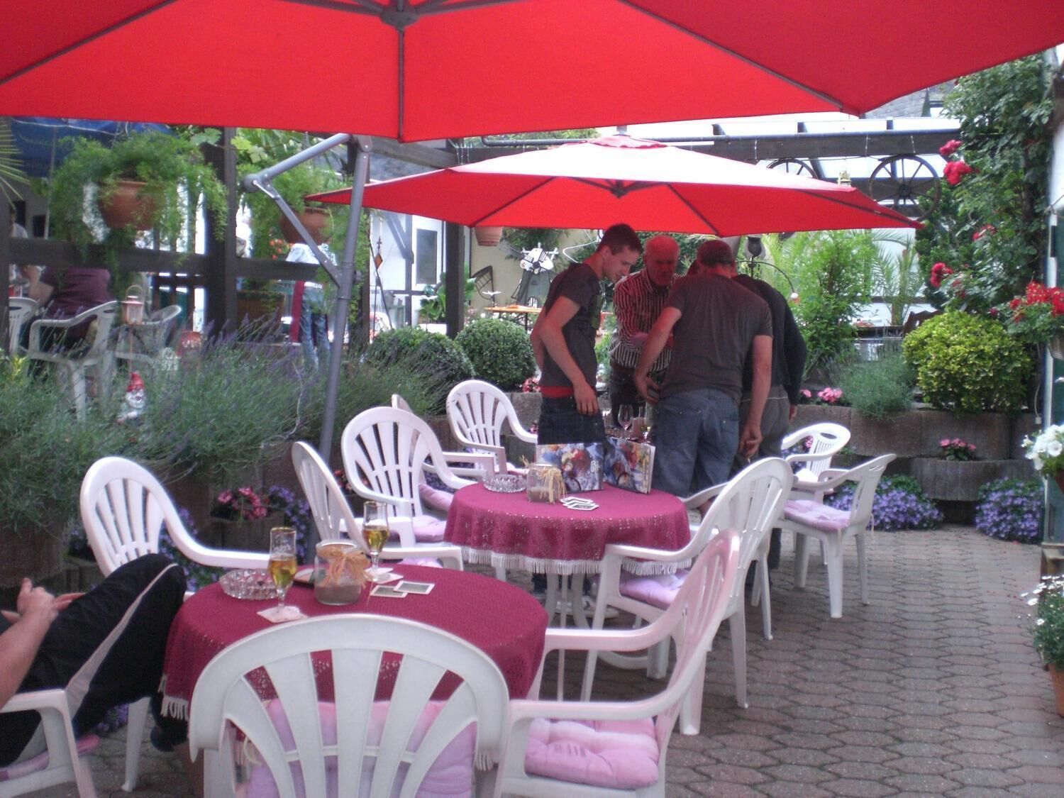 An outdoor patio area with white plastic chairs and tables, covered by red umbrellas.