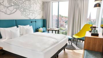 Habitación de hotel con una cama grande, un escritorio con silla, un mapa en la pared y vistas a edificios.