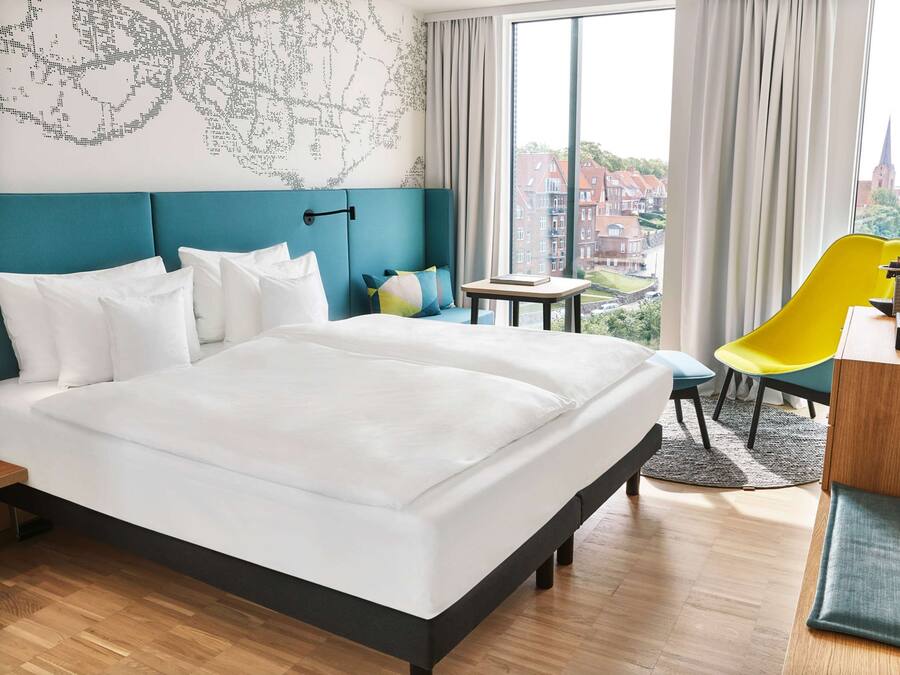 Habitación de hotel con una cama grande, un escritorio con silla, un mapa en la pared y vistas a edificios.