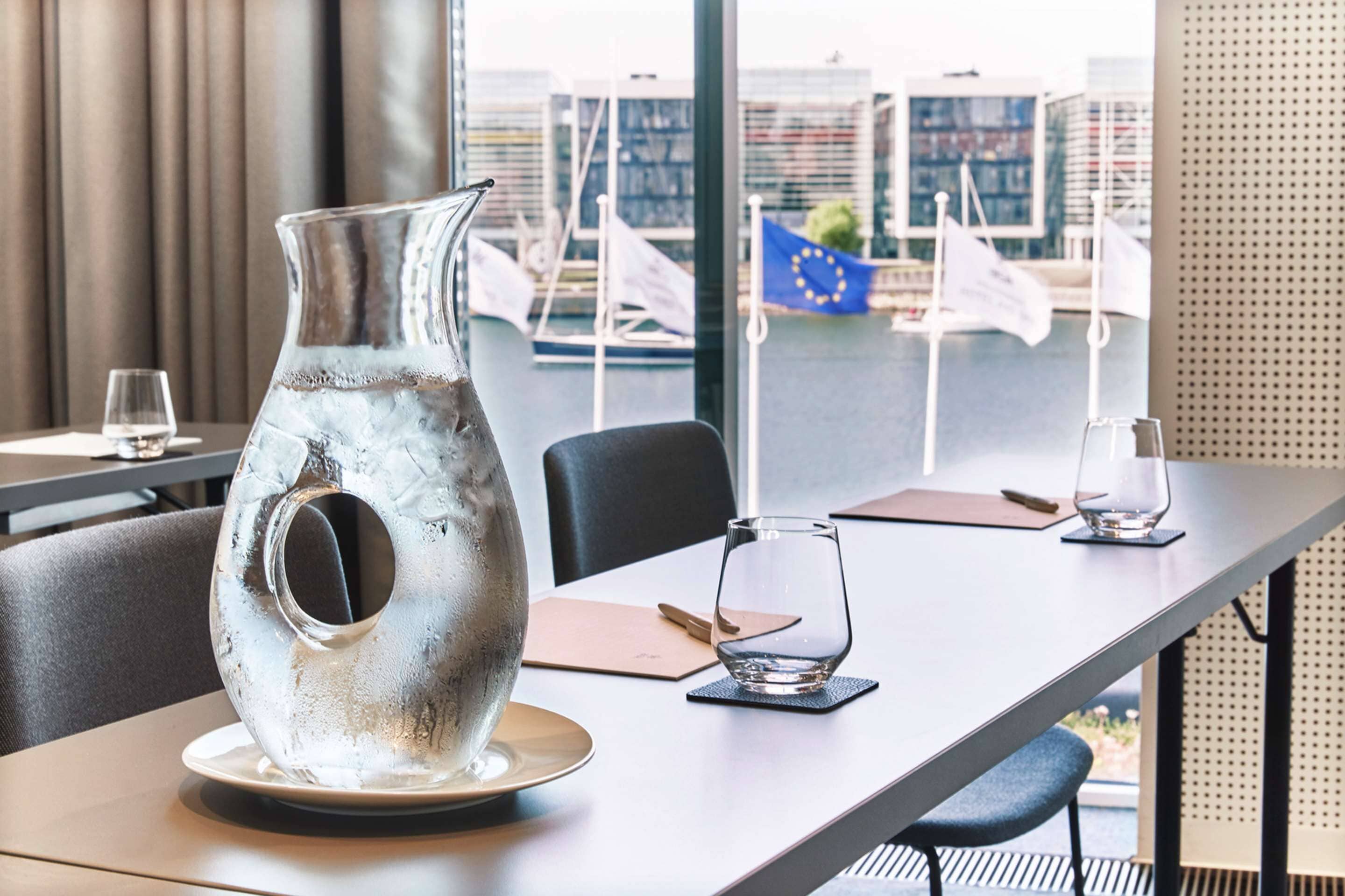 A modern dining table with a unique metallic pitcher centerpiece, a glass, and a menu.
