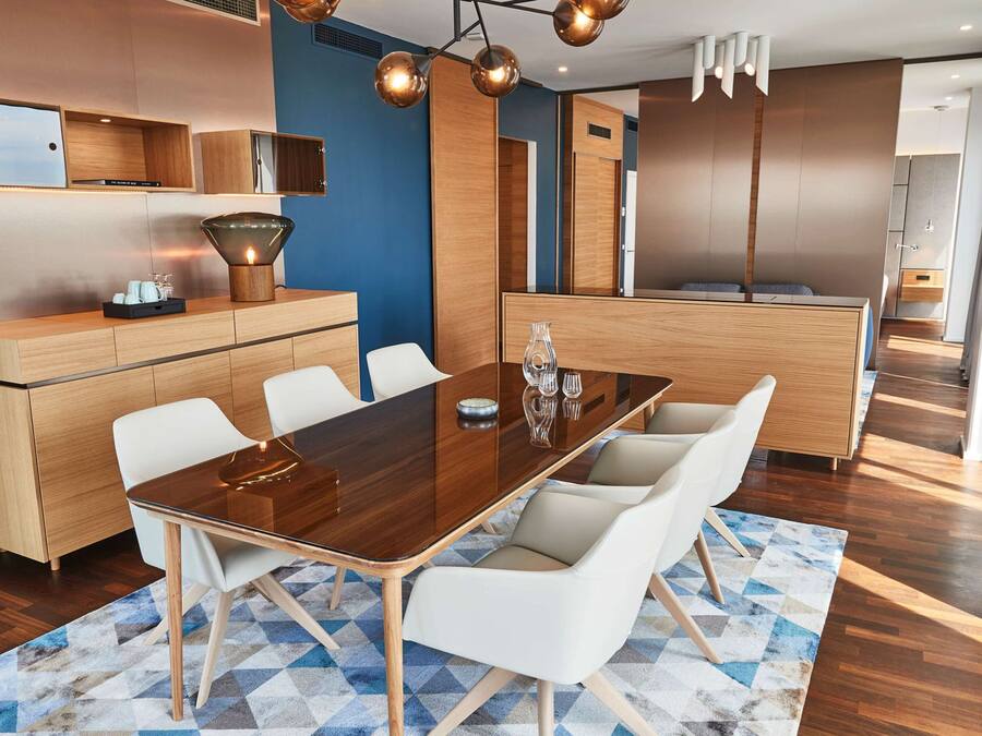 Un comedor moderno con una mesa de madera y sillas blancas, una cocina al fondo y una pared azul de acento.