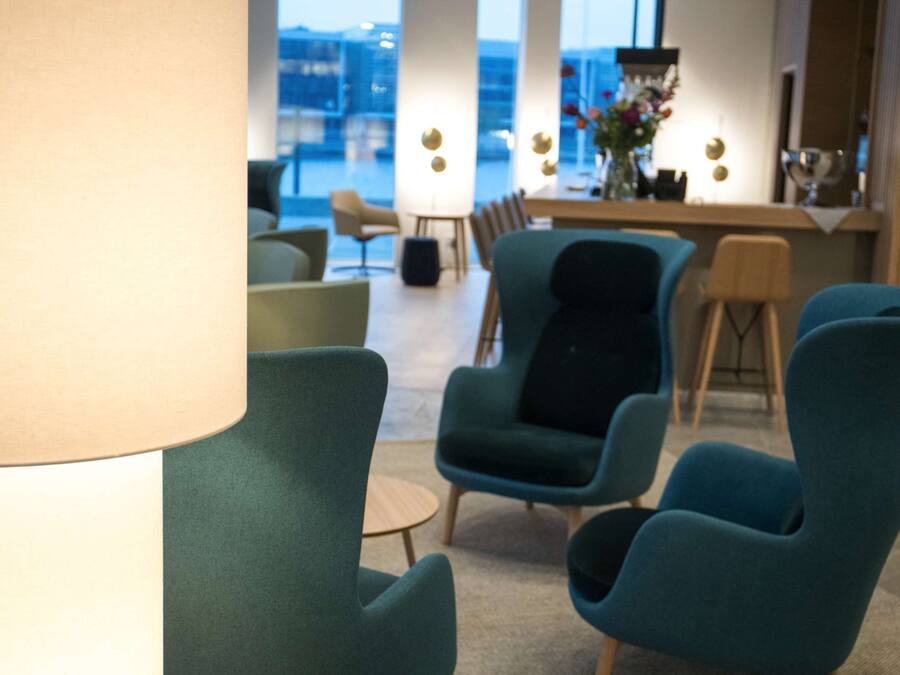 Una zona relax moderna con poltrone color petrolio, un tavolino rotondo e un bar con un vaso di fiori.