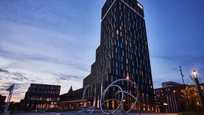 Un edificio moderno de gran altura con un llamativo letrero 'alsik' en la parte superior, rodeado de otras estructuras contemporáneas.