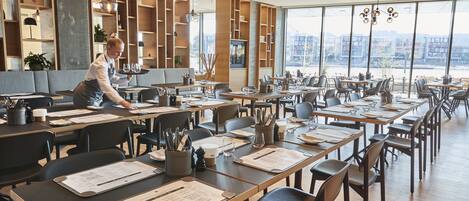 A modern restaurant with wooden furniture, large windows, and a view of the city.