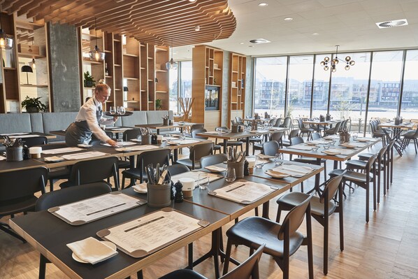 A modern restaurant with wooden furniture, large windows, and a view of the city. - Alsik Hotel & Spa (Sønderborg)