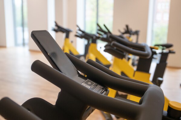 A close-up of a stationary bike with a digital display and a smartphone in hand. - Alsik Hotel & Spa (Sønderborg)