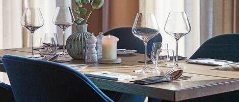 A dining table set for four with blue upholstered chairs, a white candle, salt and pepper shakers, and a vase with green leaves.