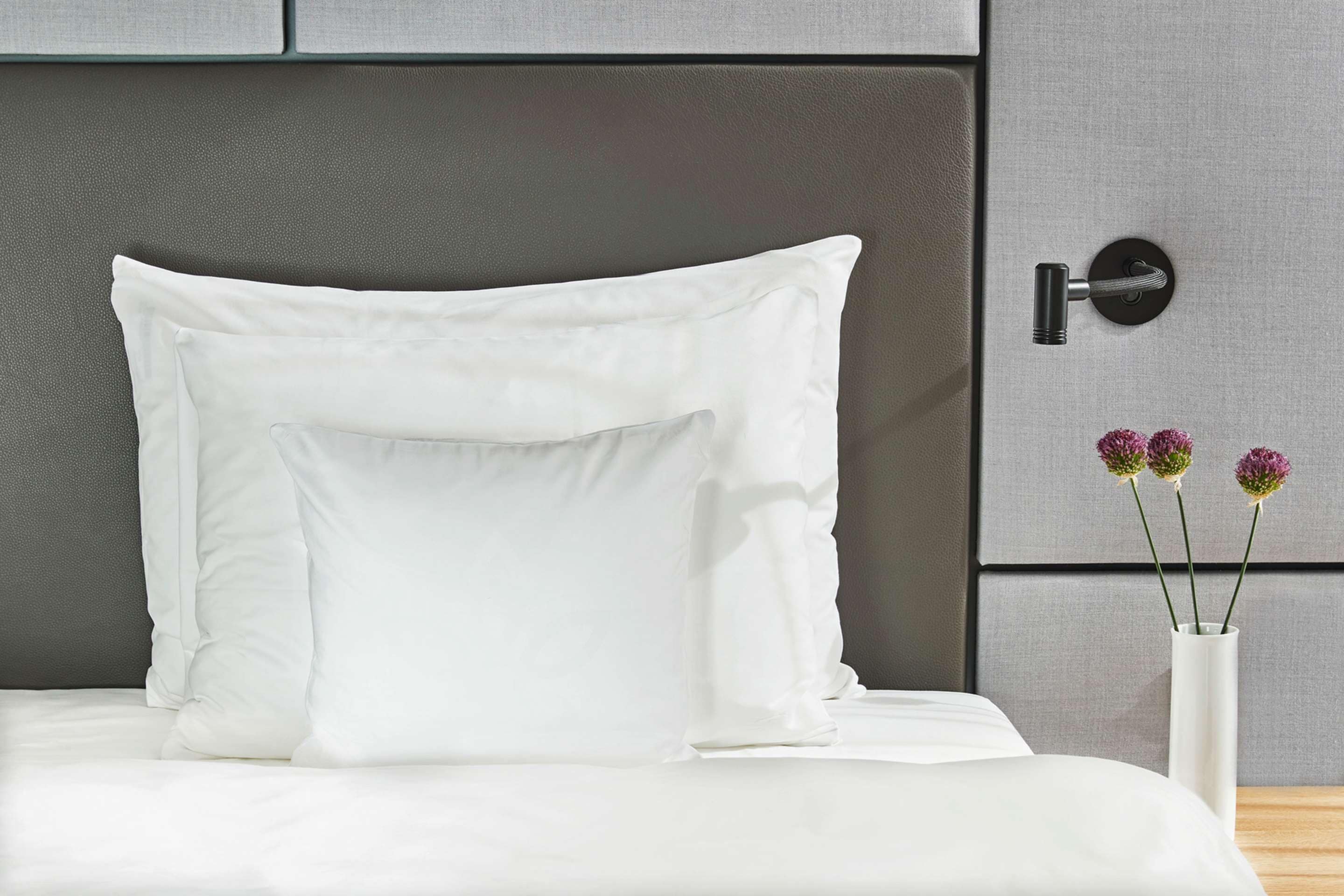 Una cama con ropa de cama blanca y un cabecero gris.