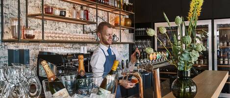 Una zona de bar con un barman, un cubo de hielo grande con la etiqueta “POL ROGER” y un jarrón con flores.