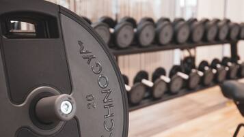 A weightlifting bench with a weight stack labeled "TECHNO" and a rack of dumbbells in the background.