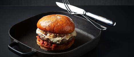 A burger in a cast iron skillet with a fork and knife beside it.