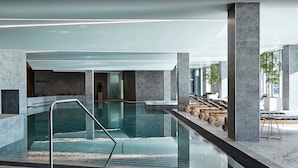 Una piscina interior moderna con paredes de vidrio transparente, una barandilla de metal y suelo de piedra.