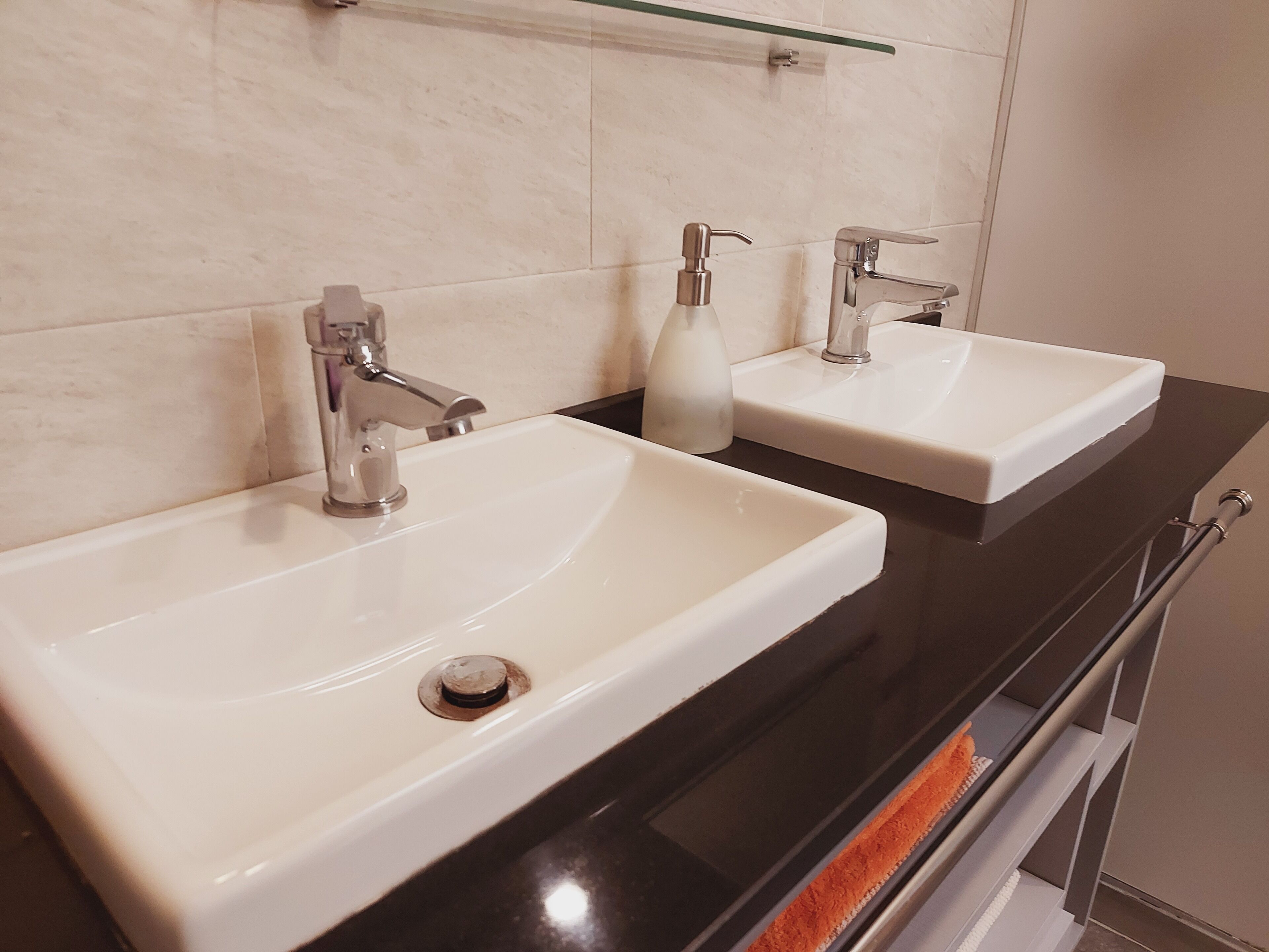 A bathroom with two white sinks, a mirror, and a glass shelf above the sink.