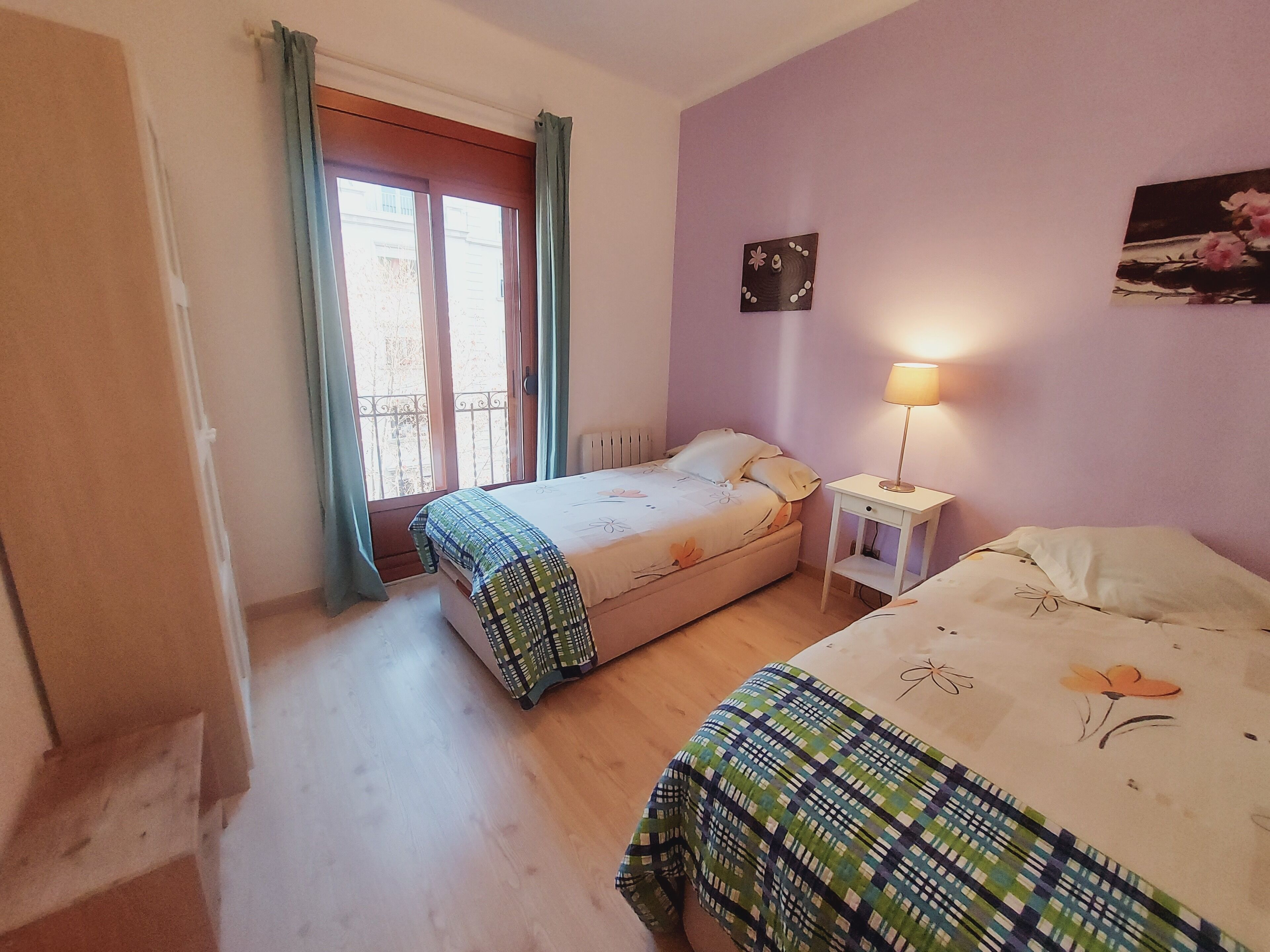 Une chambre avec deux lits, une fenêtre avec des rideaux, une table de chevet avec une lampe et un élément décoratif mural.