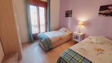 Une chambre avec deux lits, une fenêtre avec des rideaux, une table de chevet avec une lampe et un élément décoratif mural.