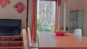 A dining area with a table, chairs, a television, and a view of a cathedral through open curtains. - Absolute Sagrada Familia (Barcelona)