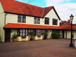 A two-story building with a red-tiled roof, multiple windows, and a brick-paved courtyard. - High Hedges Apartments (Oxford)