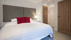 A neatly made bed with white and red bedding, a bedside lamp, and a wooden wardrobe. - High Hedges Apartments (Oxford)