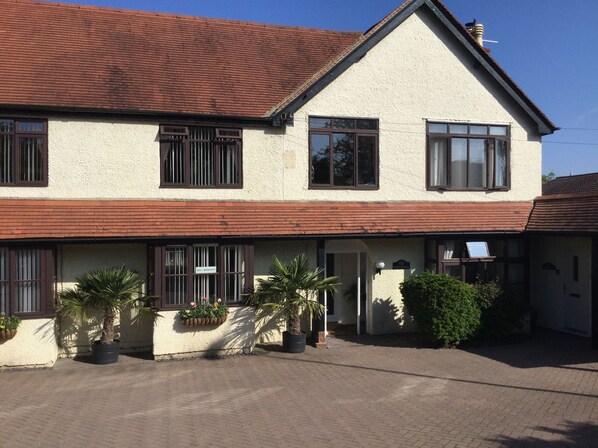 A two-story building with a red-tiled roof, a white facade, and multiple windows with brown frames. There are potted plants in front of the building. - High Hedges Apartments (Oxford)