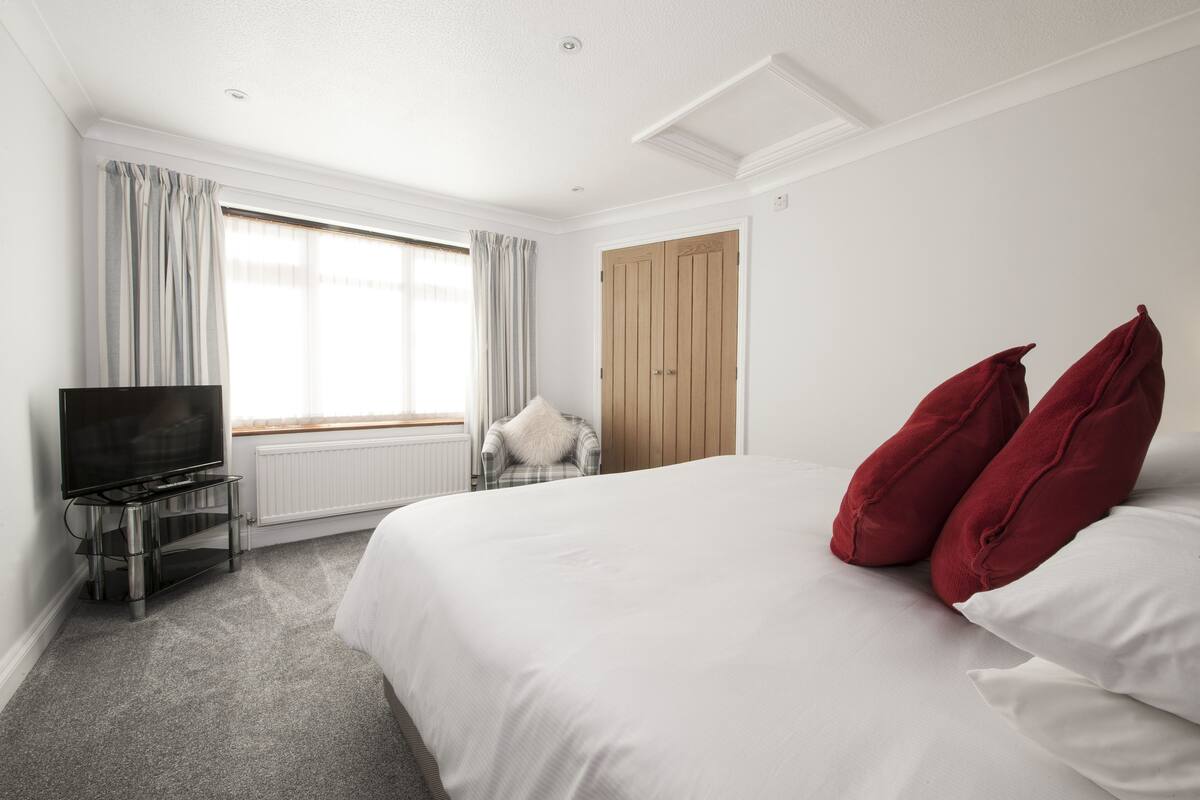 A hotel room with a bed, a TV, a chair, and a window with curtains.