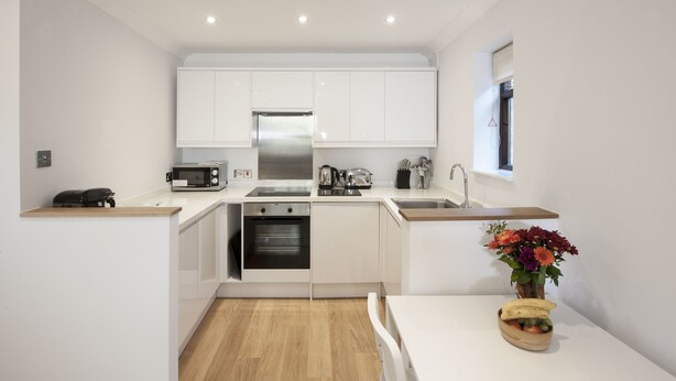 A compact kitchen with white cabinetry, a built-in oven, a microwave, and a sink. - High Hedges Apartments (Oxford)
