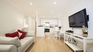 A modern living room with a sofa, a TV on a stand, and a kitchen in the background. - High Hedges Apartments (Oxford)