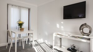 A modern hotel room with a white desk, two chairs, a TV mounted on the wall, and a console table with a decorative item and a remote control. - High Hedges Apartments (Oxford)