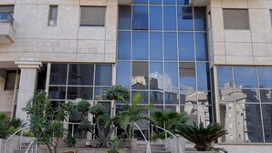A modern building with a reflective glass facade, multiple balconies, and a central staircase leading to the entrance.