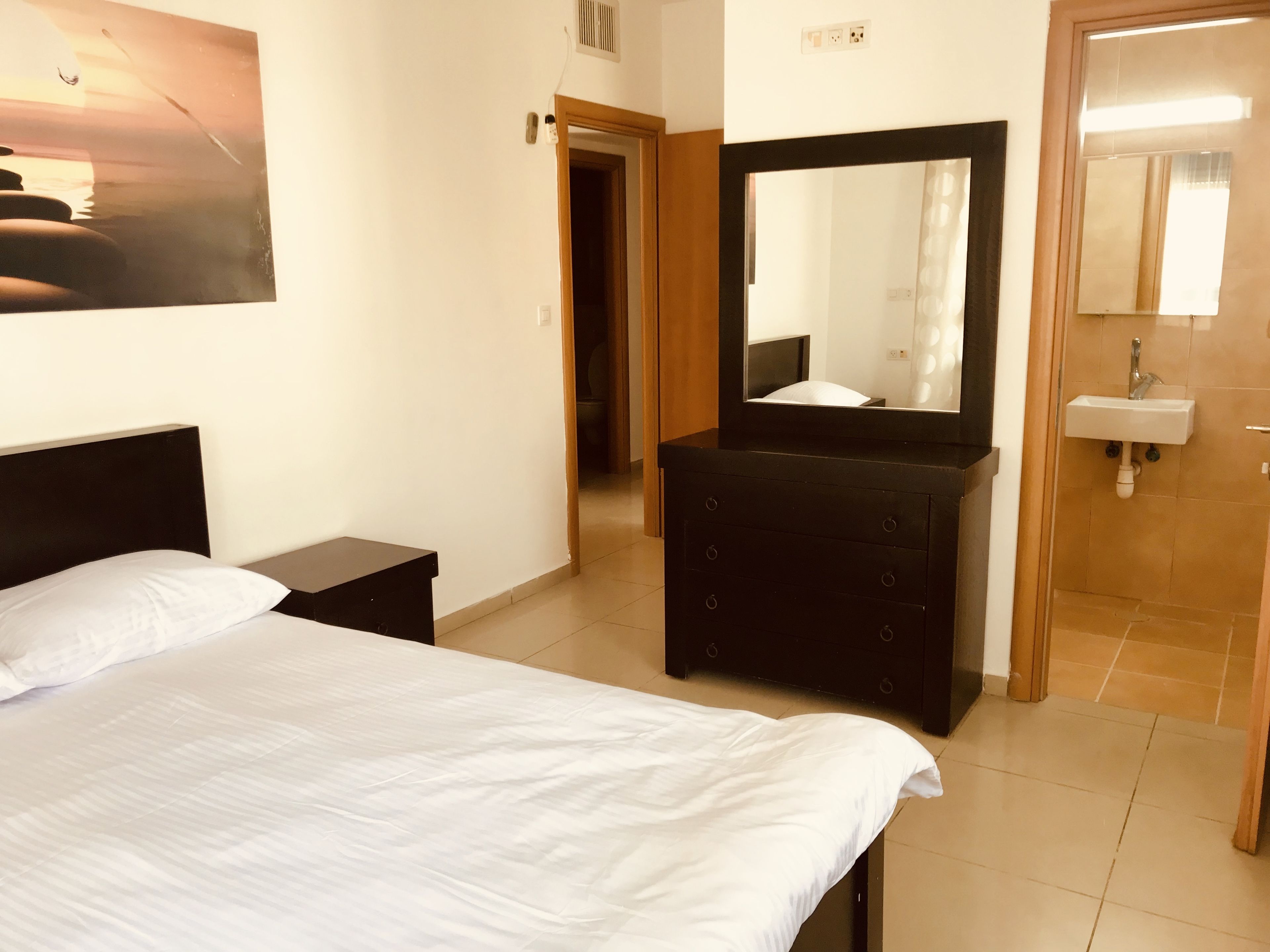 Une chambre à coucher avec un lit, une commode, un miroir et une salle de bain visible à travers une porte ouverte.