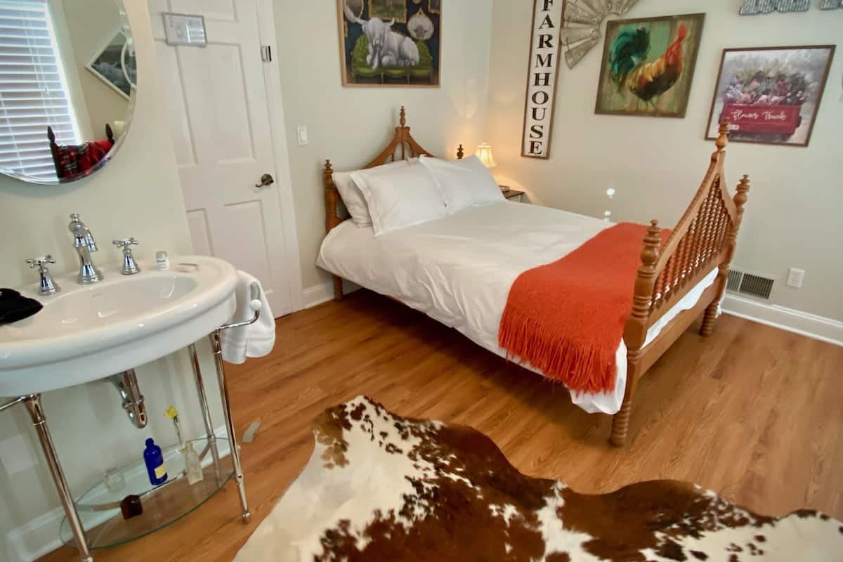 A bedroom with a wooden bed, a white bedside table, a mirror, a white sink, and a cowhide rug.
