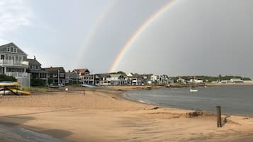 Una playa con casas al fondo y un arcoíris en el cielo.